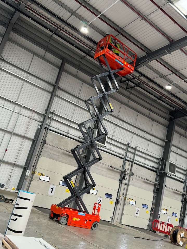 An engineer working from a raised scissor lift inside a large industrial unit.