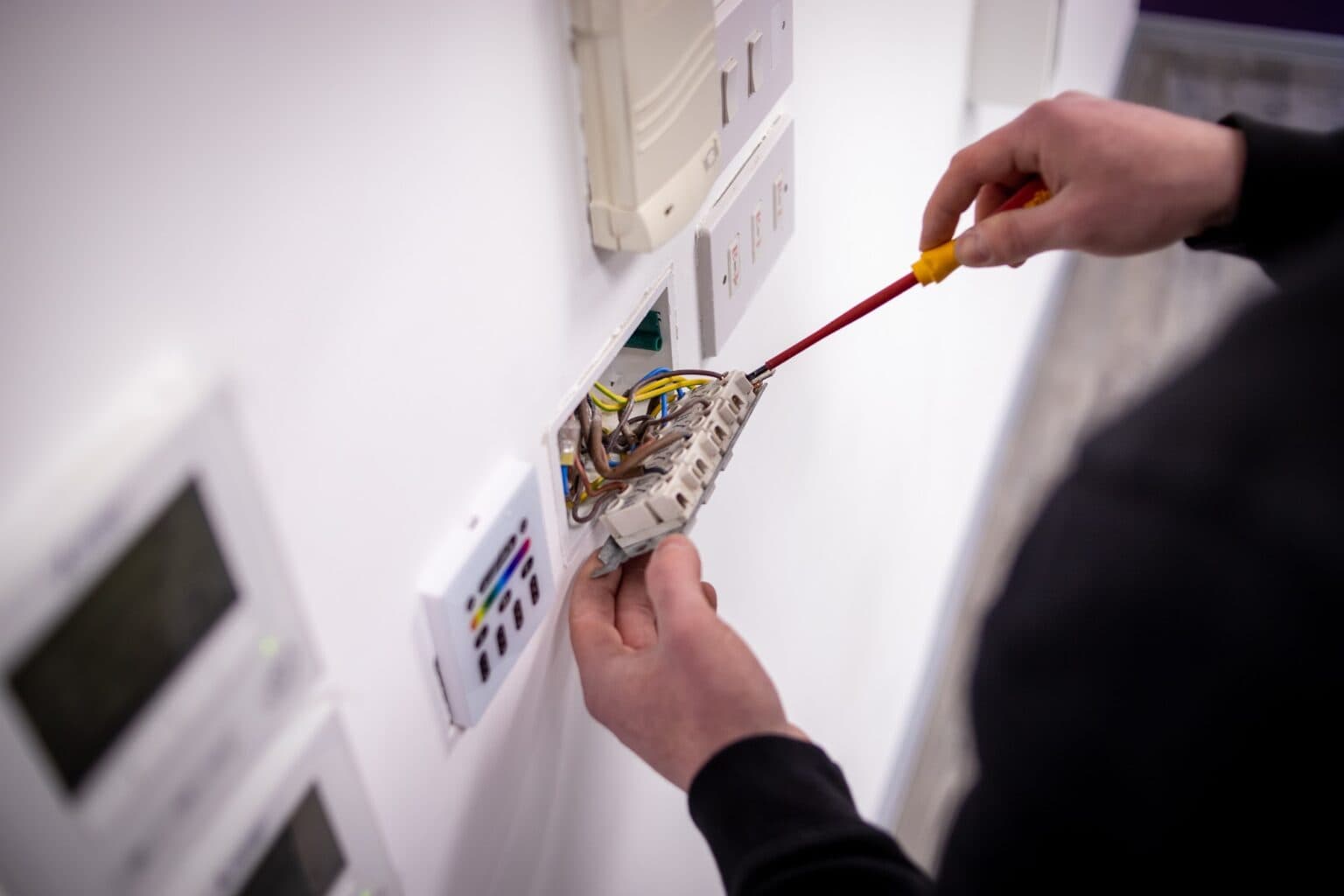 An electrician using a screwdriver to work on wiring inside an open wall socket back box.